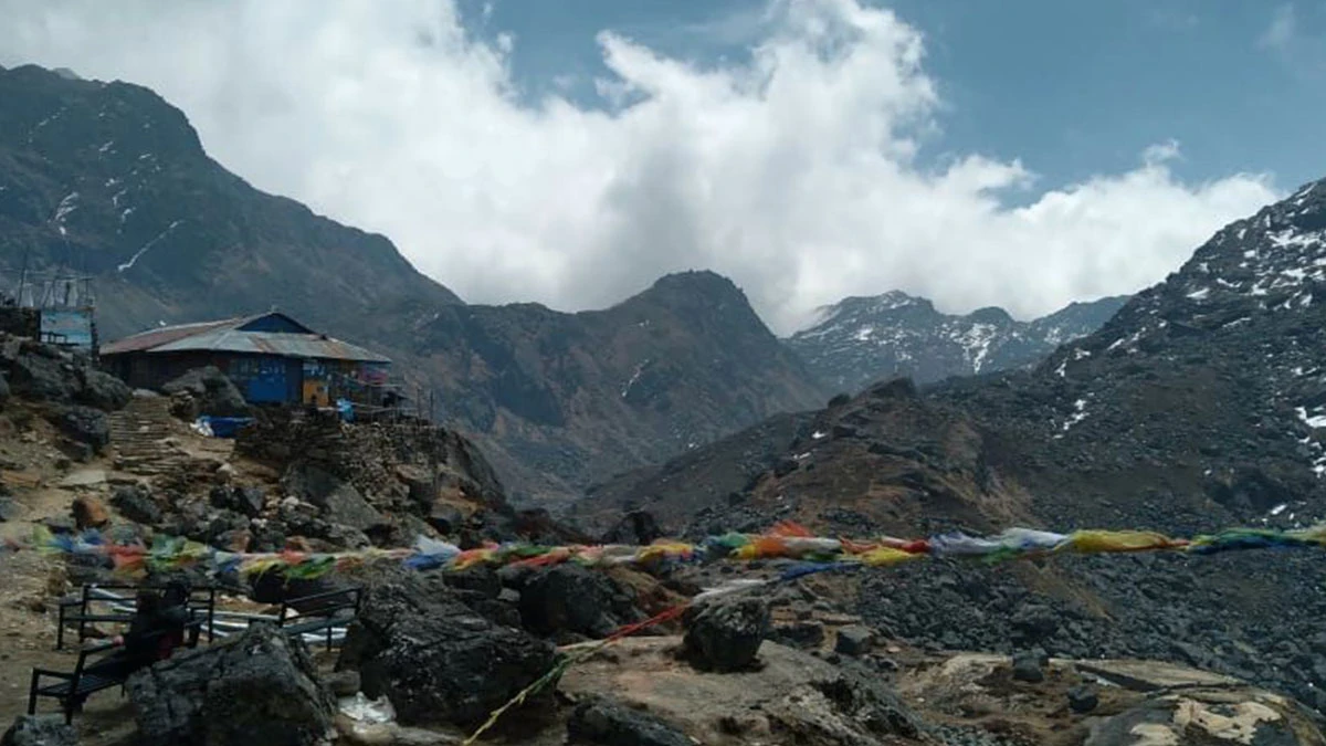 Teahouse in rocky mountains with prayer flags fluttering, clouds and snow peaks in Langtang Valley Trek, Nepal Himalayas.
