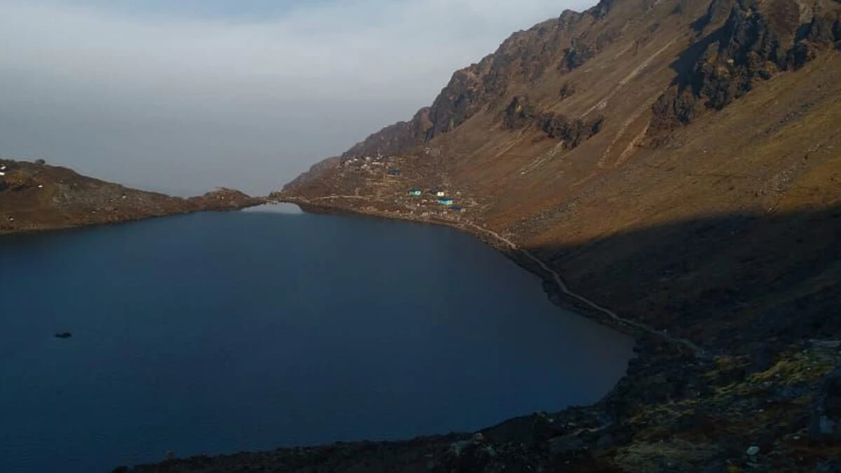 Teahouse beside large alpine lake surrounded by towering mountains on Langtang Valley Trek, Nepal Himalayas.